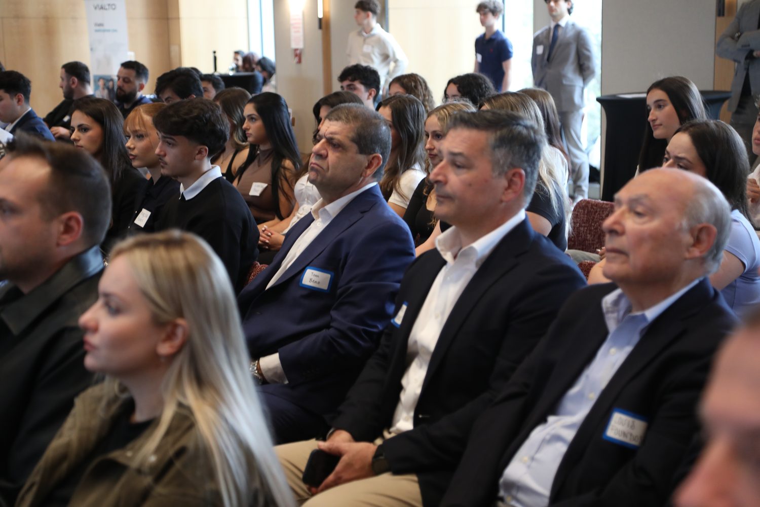 Attendees in the audience wearing name badges during the opening remarks.