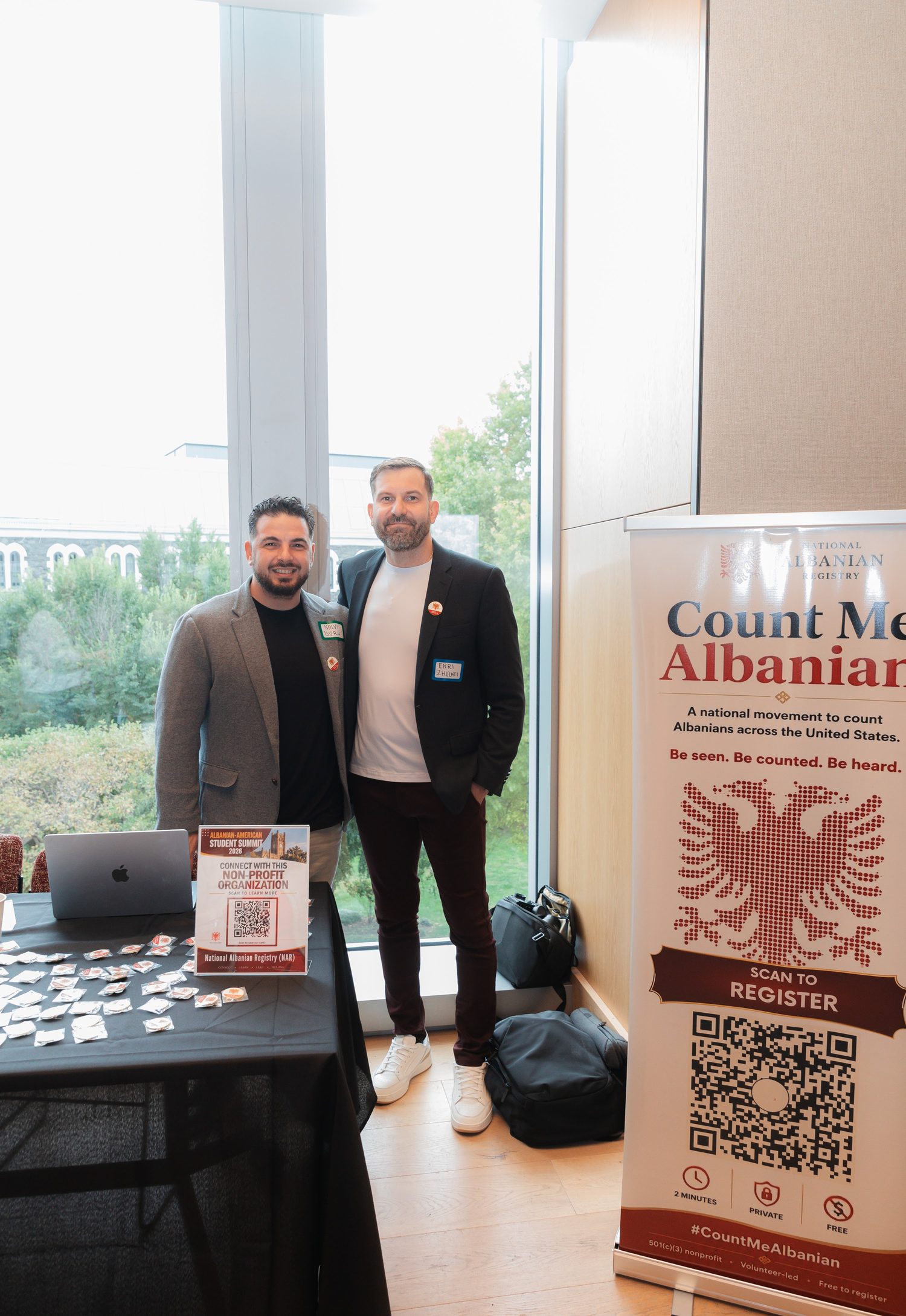 Two organizers beside the National Albanian Registry banner and the sign-in table by the windows.