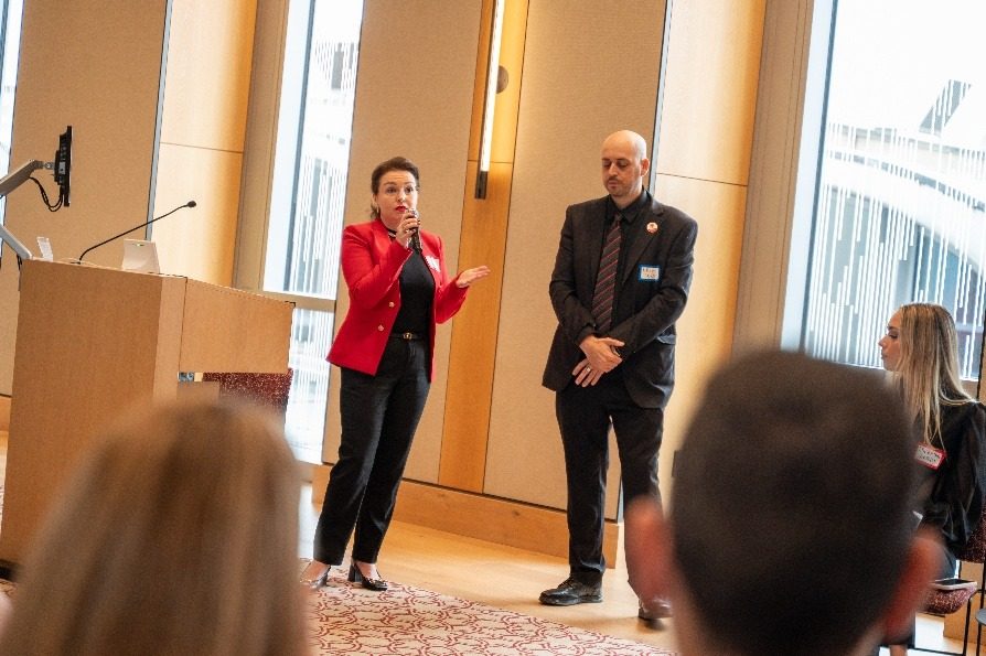 An organizer speaking from the lectern with a colleague standing beside her.