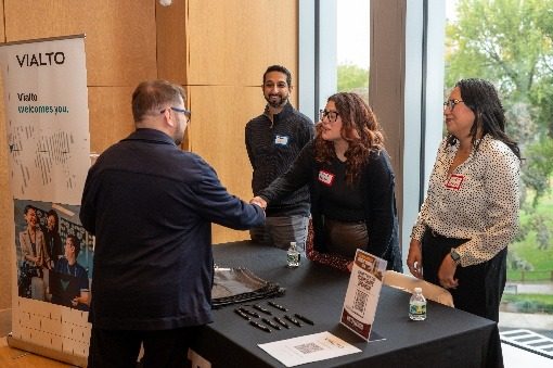 A Vialto Partners representative shaking hands with an attendee at the sponsor table.